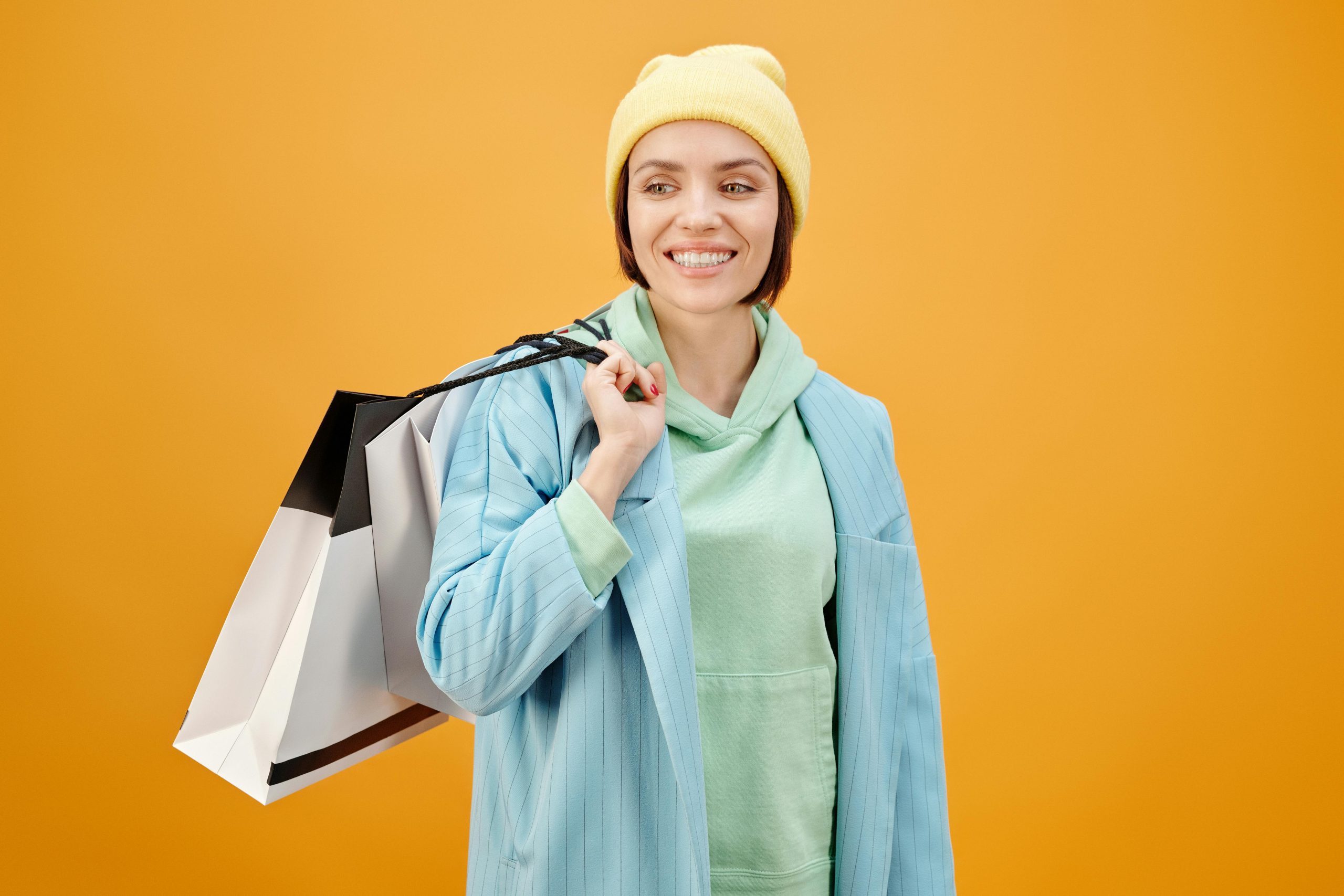 Smiling woman in casual attire holding shopping bags with a vibrant yellow background.