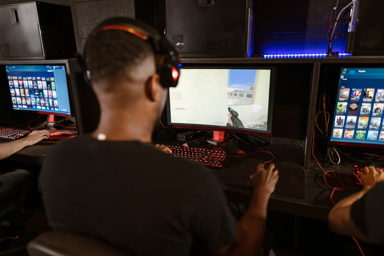 A man deeply engaged in a video game at a modern esports setup with multiple screens.